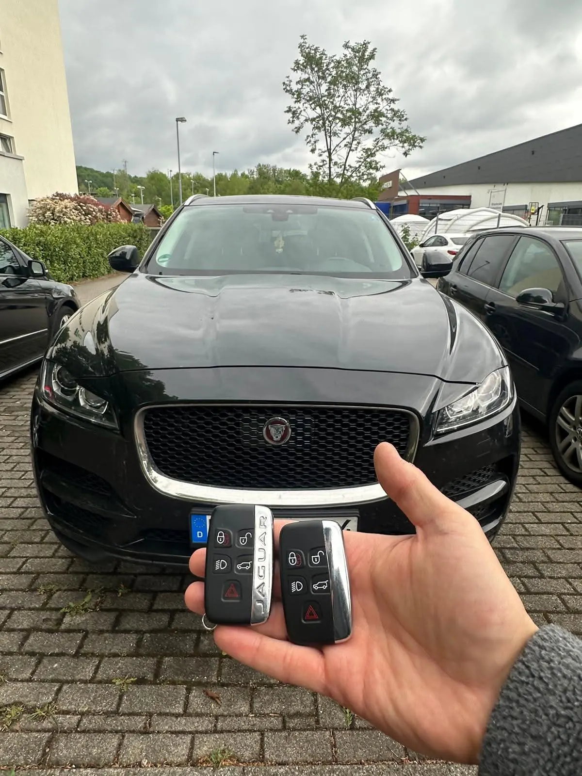 Zwei Jaguar-Keyless-Schlüssel vor einem schwarzen Jaguar F-Pace
