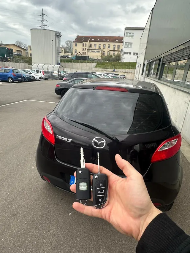Zwei Klappschlüssel vor einem schwarzen Mazda 2